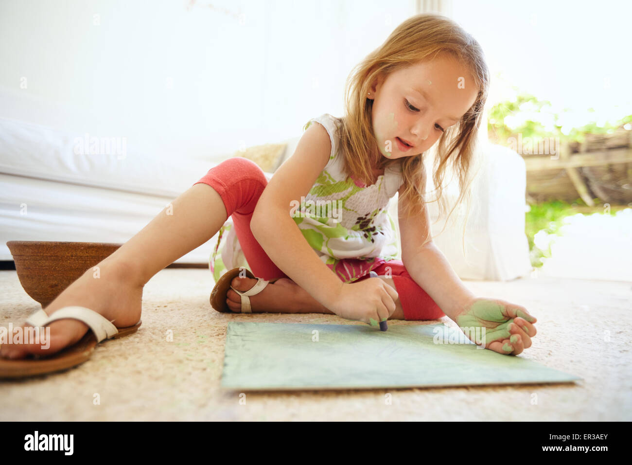 Colpo di piccolo grazioso Baby girl colorazione immagine mentre è seduto sul pavimento a casa. Foto Stock