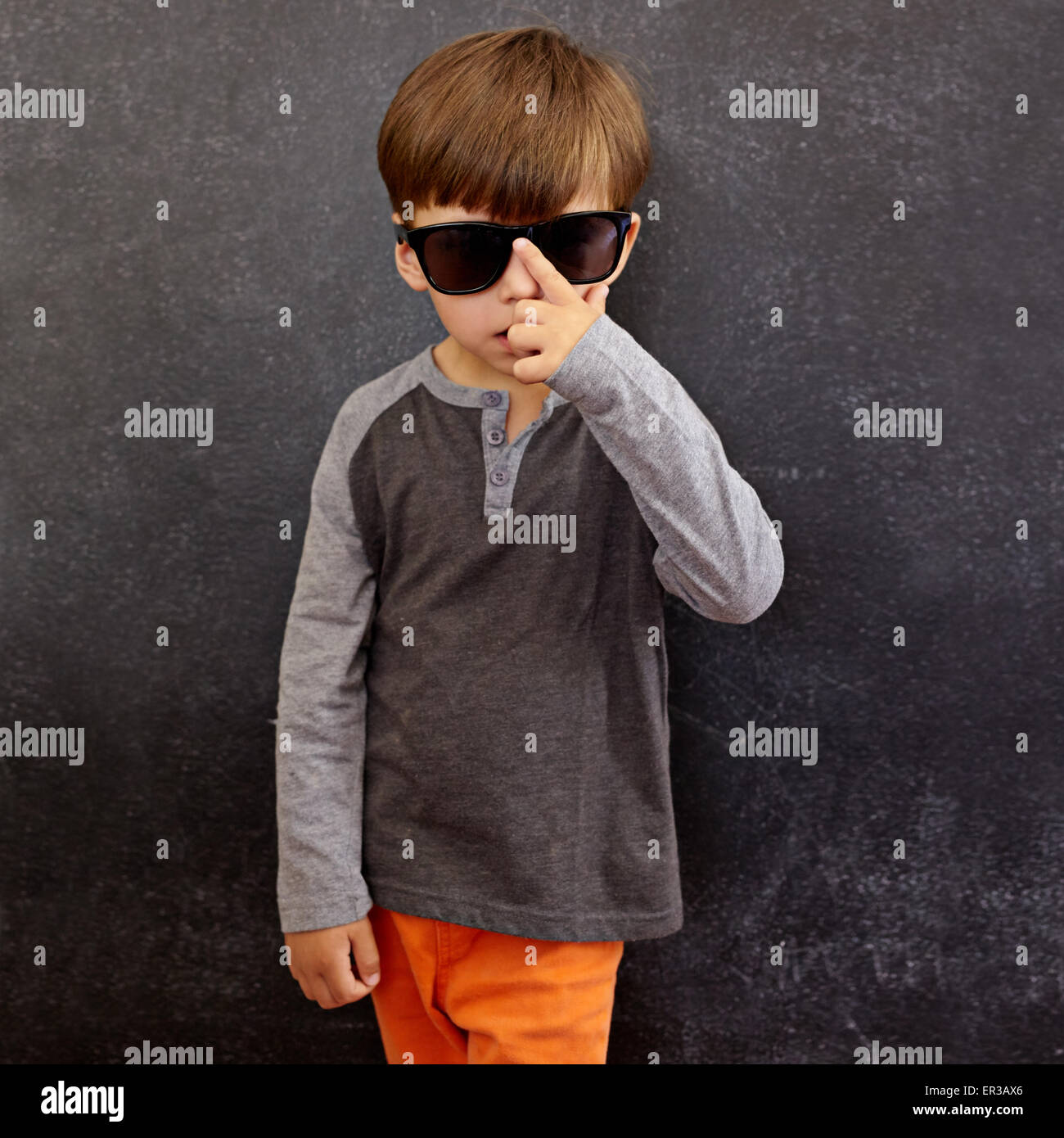 Ritratto di Little Boy indossando occhiali da sole guardando la fotocamera. Piccolo bambino di fronte a una lavagna adegua la sua tonalità. Foto Stock