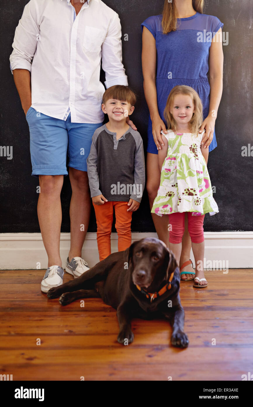 Ritagliato colpo di bella giovane famiglia con il loro cane. Il Labrador retriever seduto sul pavimento con i bambini ed i loro genitori in piedi Foto Stock