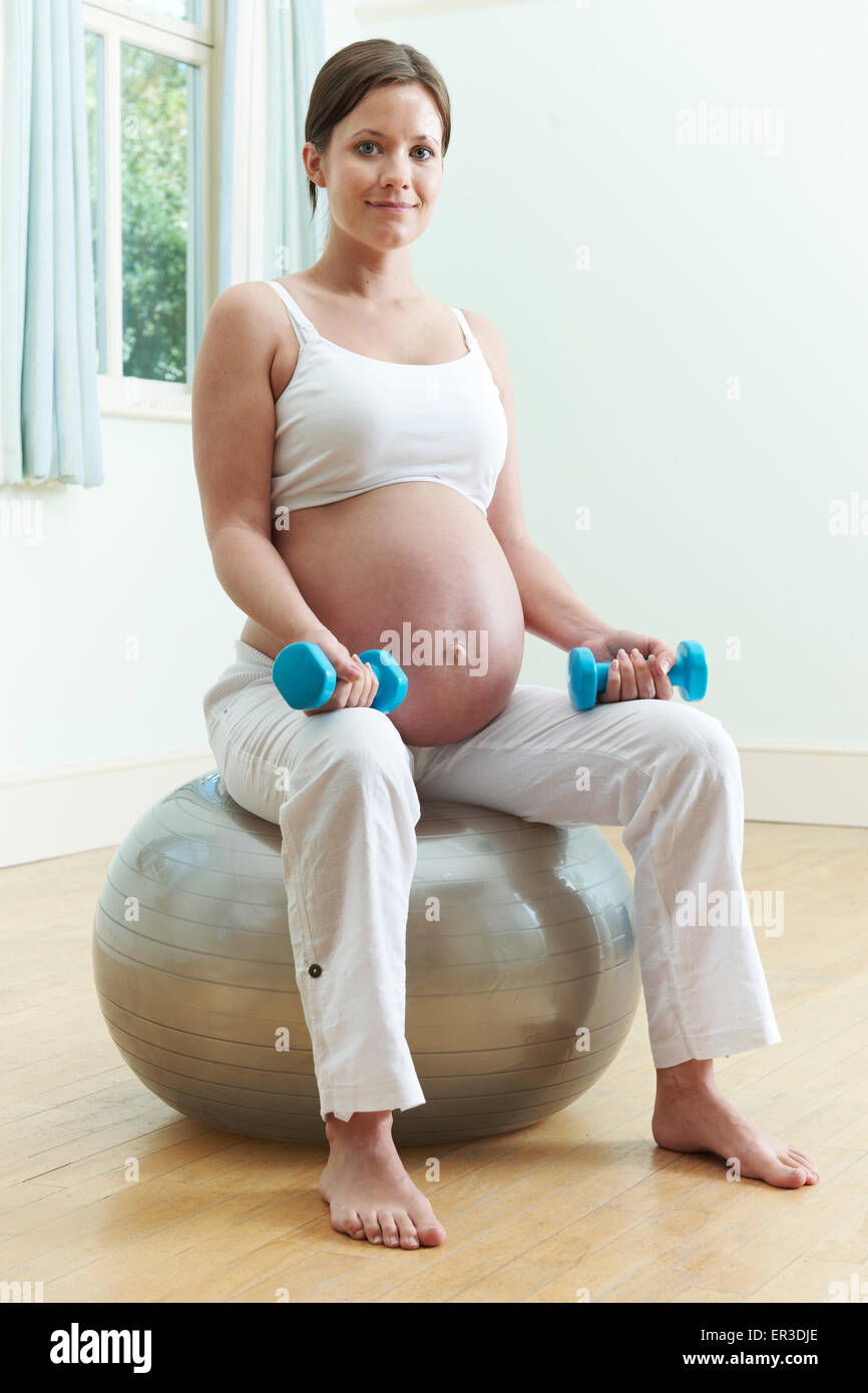 Donna incinta seduta su palla ginnica con pesi Foto Stock