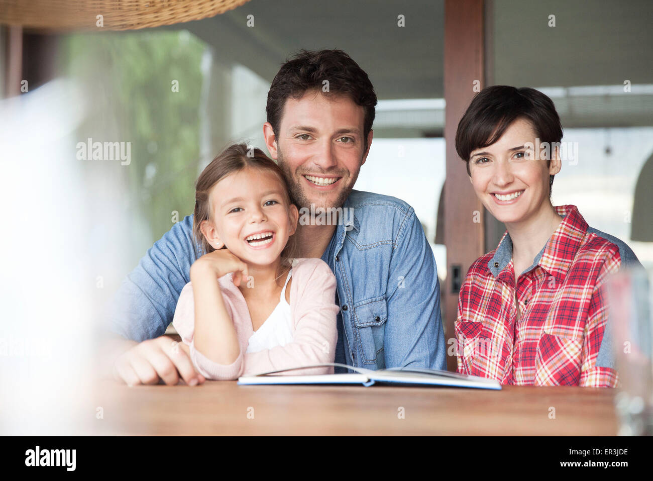 Famiglia seduti insieme a tavola con libro aperto, ritratto Foto Stock