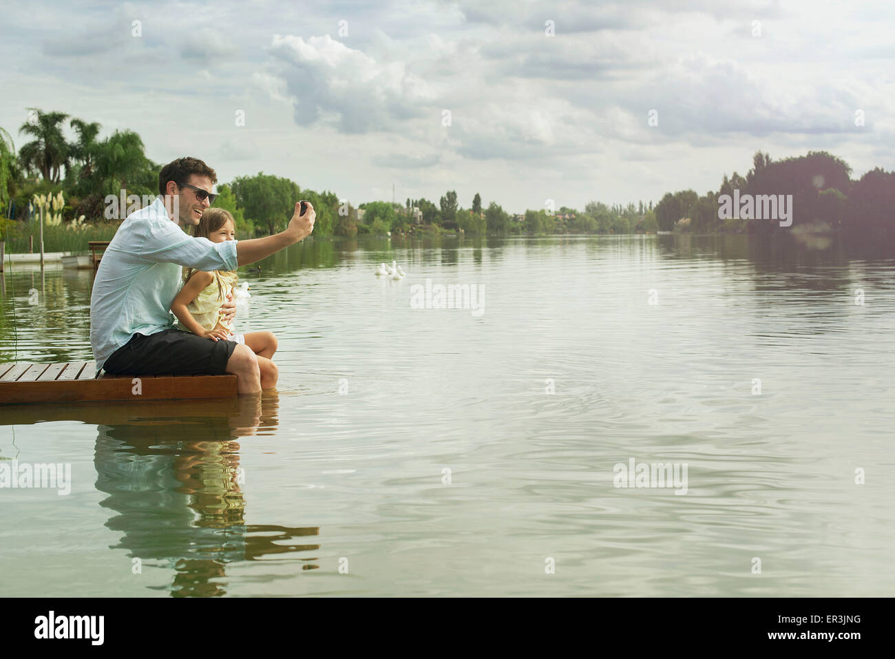 Padre e figlia seduti sul dock tenendo selfie Foto Stock