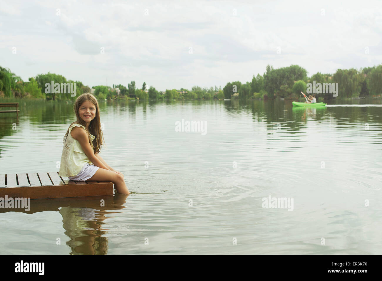 Ragazza seduta sul dock con piedi penzolanti nel lago, ritratto Foto Stock