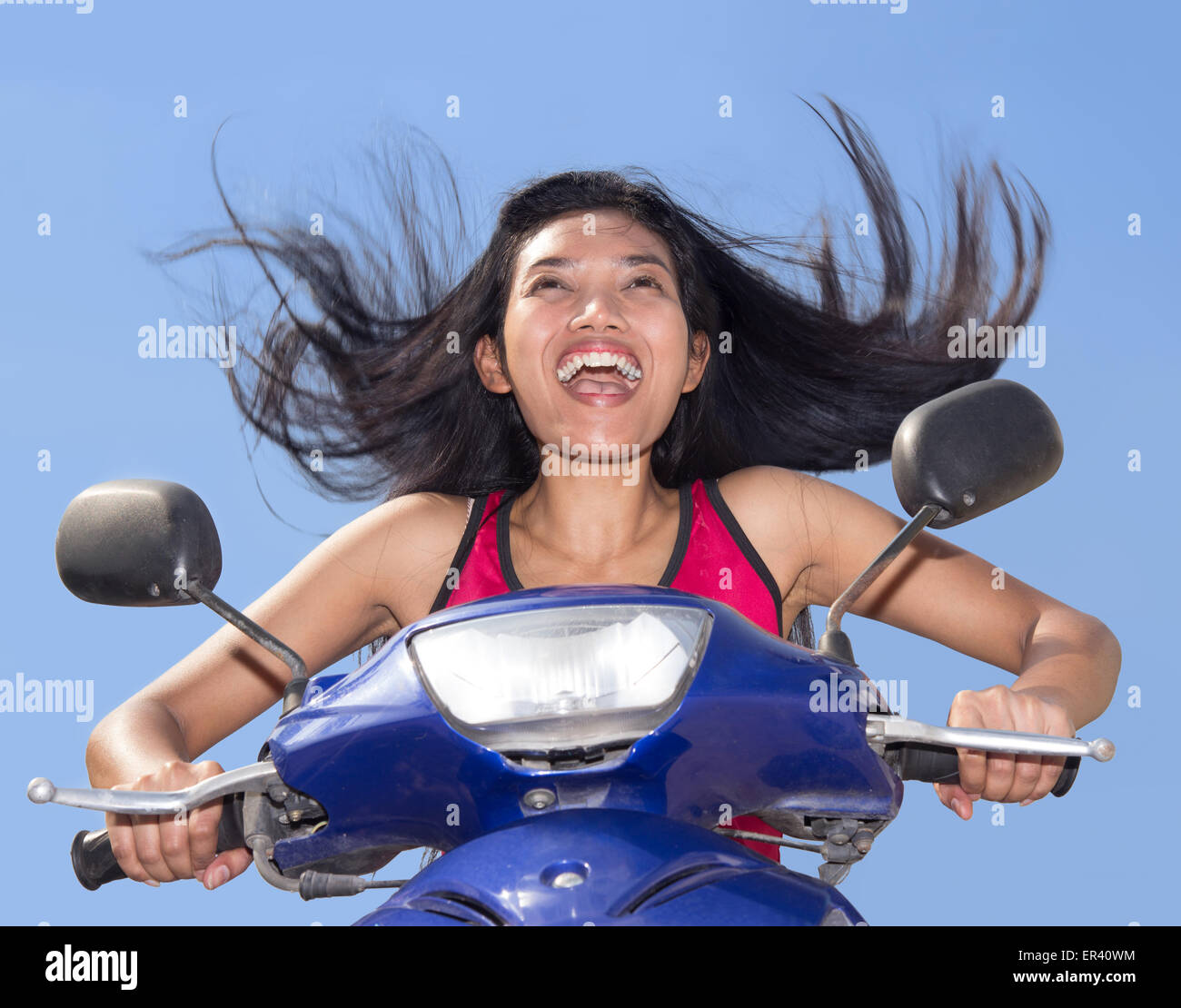 Donna con capelli volanti in sella a una moto su uno sfondo blu Foto Stock