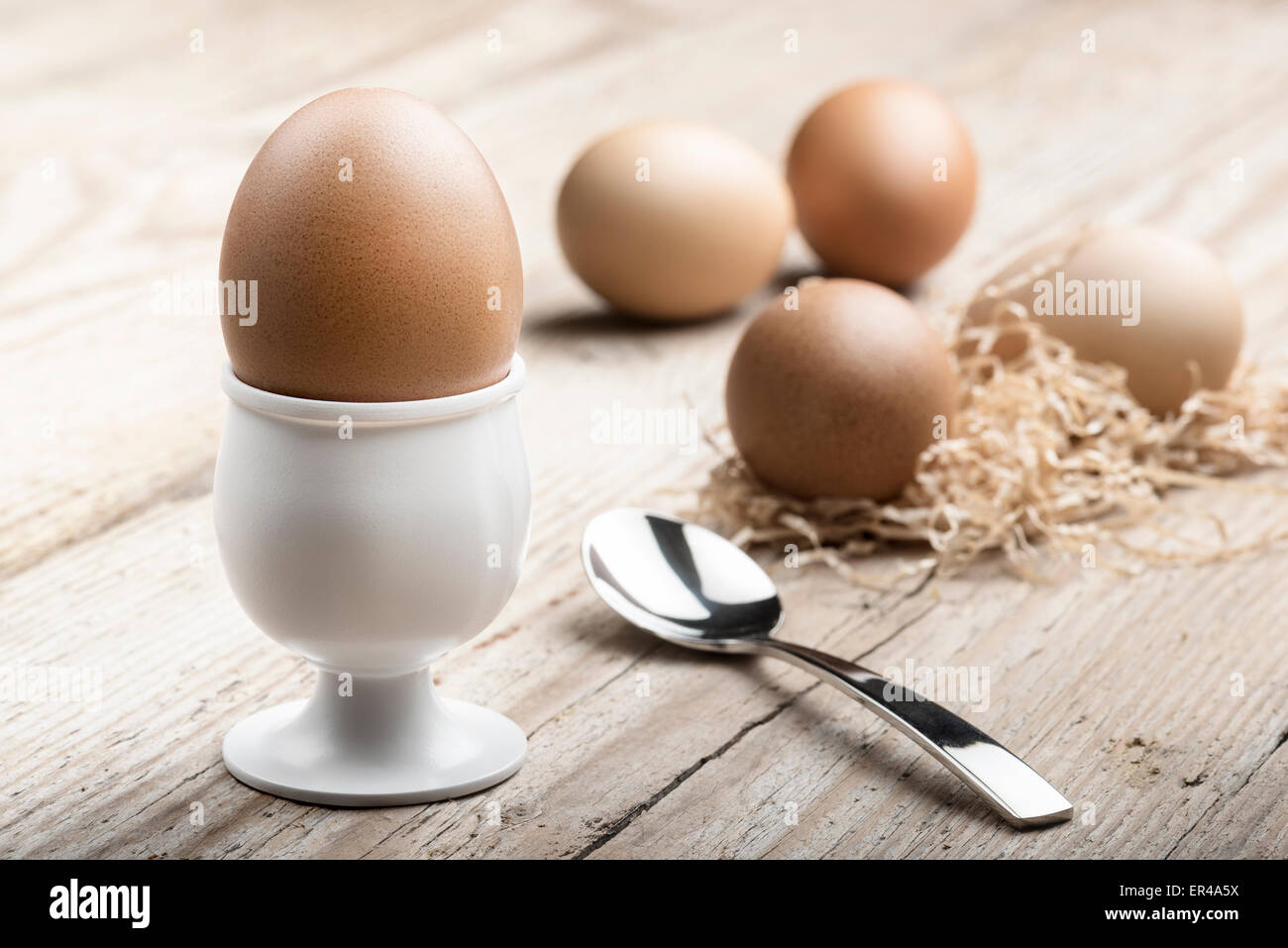 Eggcup con cucchiaino e uova sode, sul tavolo di legno Foto Stock