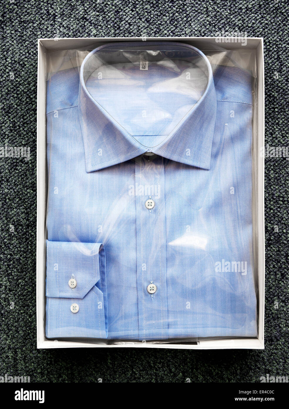 Angolo di Alta Vista di Tailor made Blue Button Down Dress shirt avvolte nel cellophane e piegato a scatola aperta sulla superficie ricoperta con moquette Foto Stock