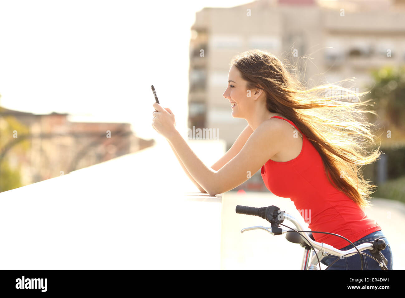 Profilo di un adolescente ragazza utilizzando un telefono cellulare in un parco in una soleggiata giornata estiva con vento muovendo i suoi capelli Foto Stock