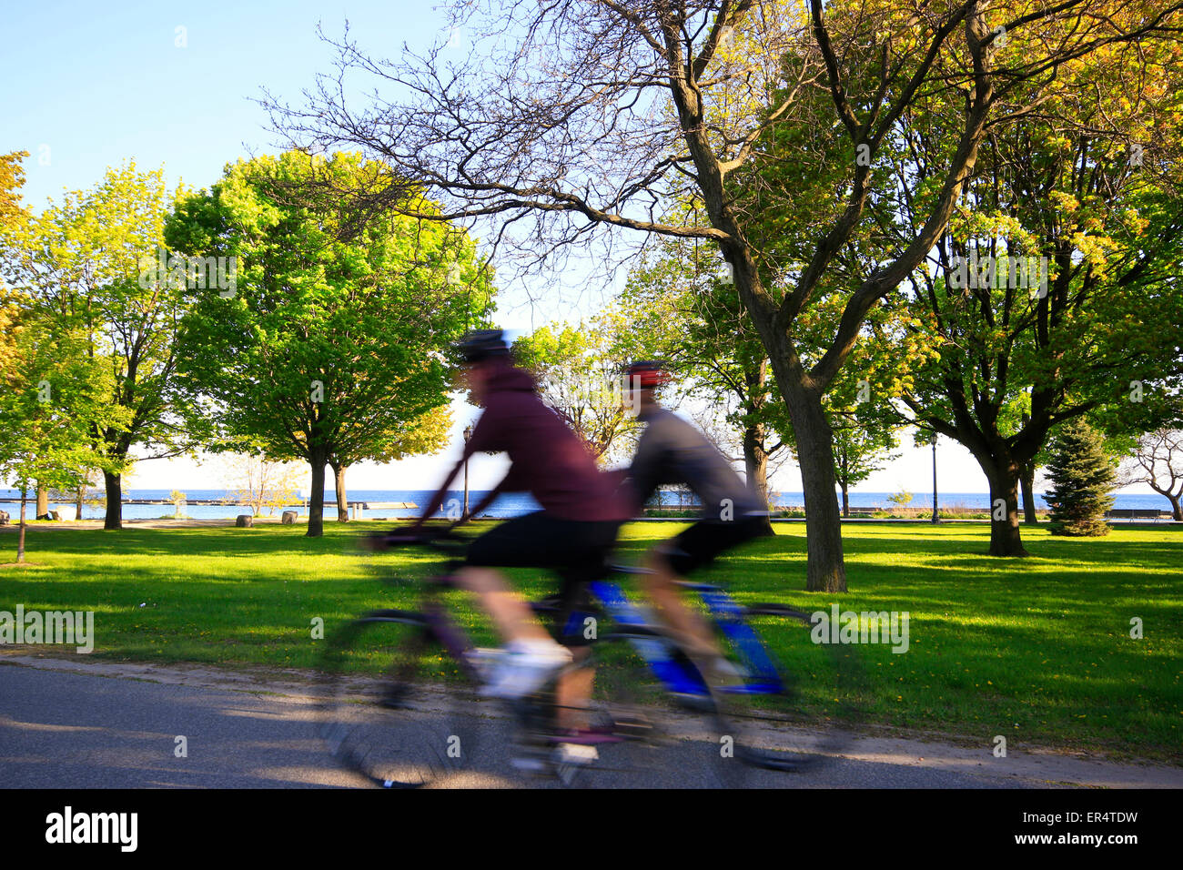 Motion offuscata e irriconoscibili le persone di sesso femminile in bicicletta lungo il sentiero sul lungomare nei pressi di Humber Bay a Etobicoke, Toronto, Ontario, C Foto Stock