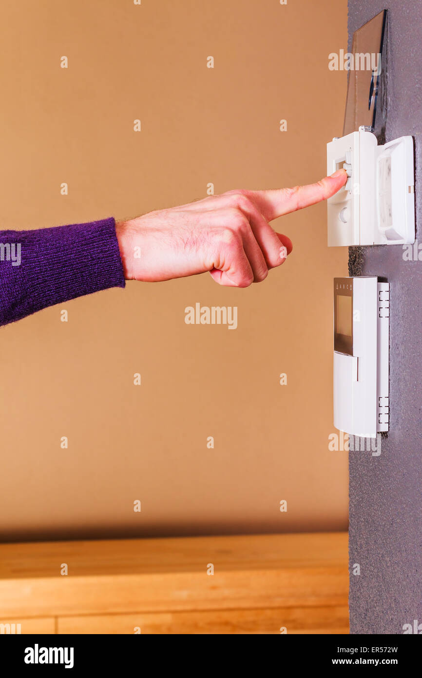 Giovane Maschio lato premendo il pulsante del termostato elettronico sulla parete della casa moderna. Pulire scena di sfondo viola maglione di lana. Foto Stock