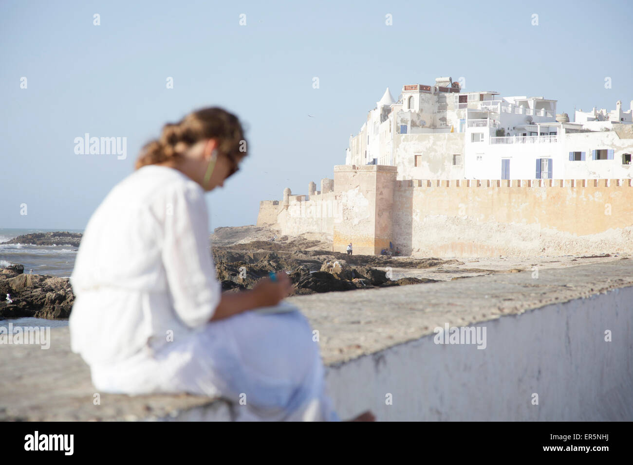 Donna seduta su una parete, Essaouira, Marocco Foto Stock