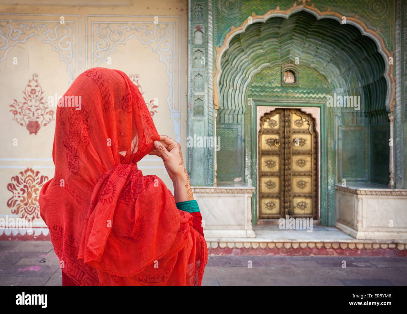La donna in sciarpa rossa guardando il cancello verde porta in palazzo di città di Jaipur, Rajasthan, India Foto Stock