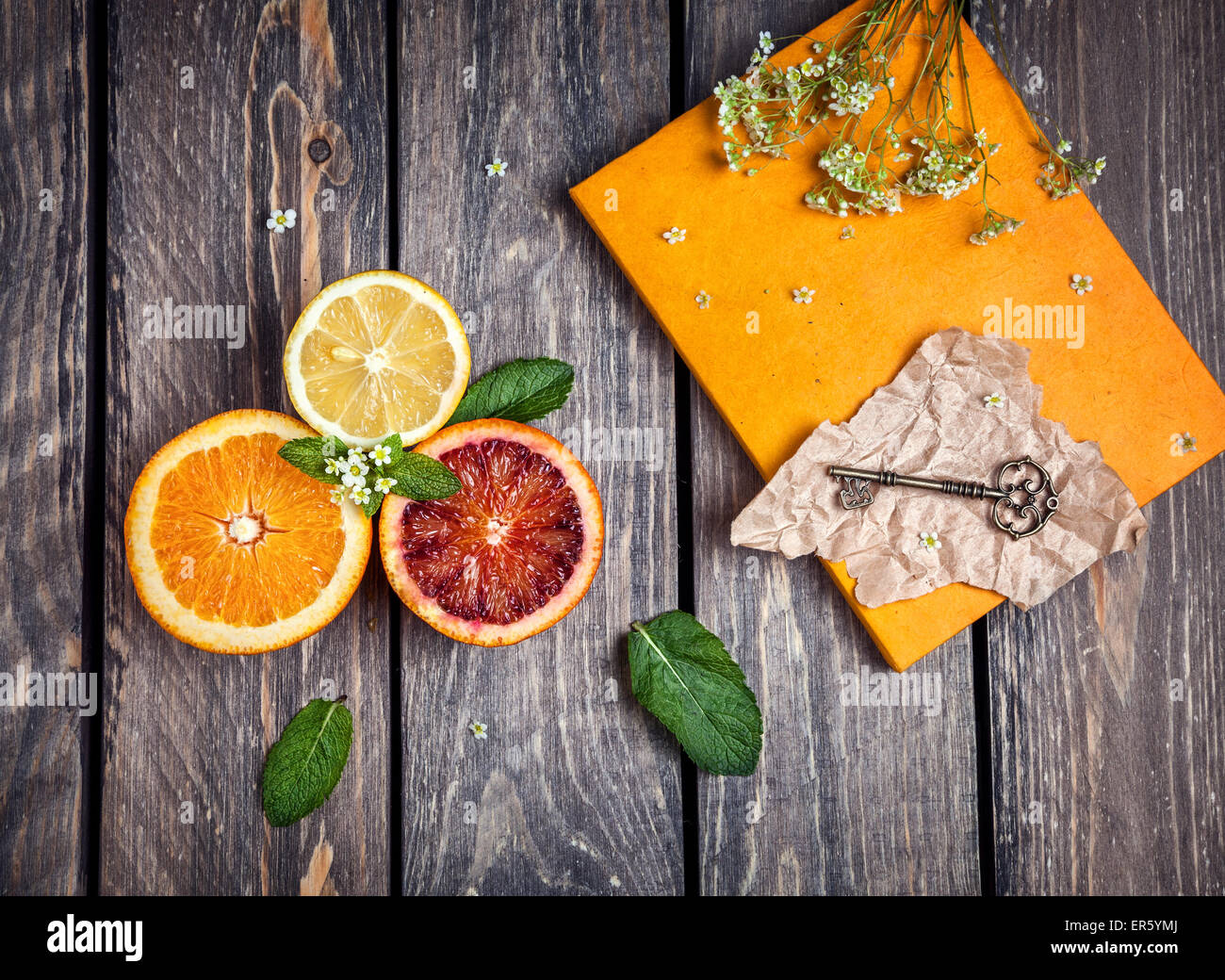 Arance, limone, giallo notebook, chiave e fiori bianchi a sfondo di legno Foto Stock
