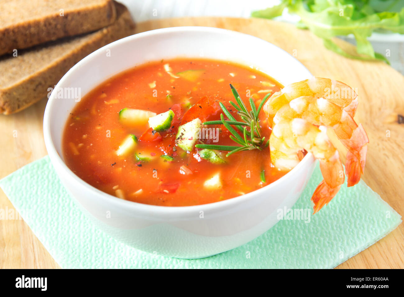 Deliziosi piatti gustosi piatti di verdura fredda zuppa di pomodoro gazpacho con gamberi (gamberetti) e rosmarino in vaso bianco su sfondo di legno, chiudi Foto Stock