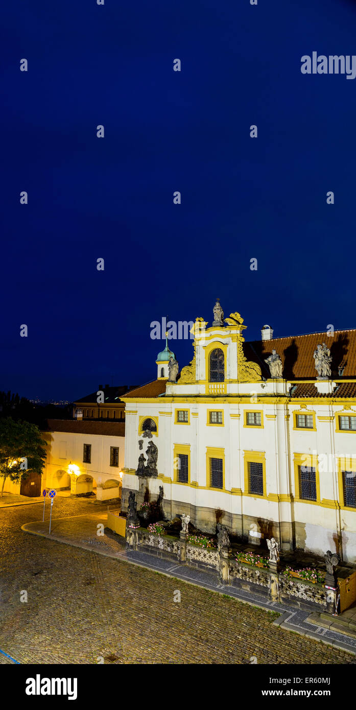 Vista notturna della facciata della Chiesa Loreta a Praga: tetto verde su bianco campanile, pareti di colore bianco, rosso sul tetto. Foto Stock