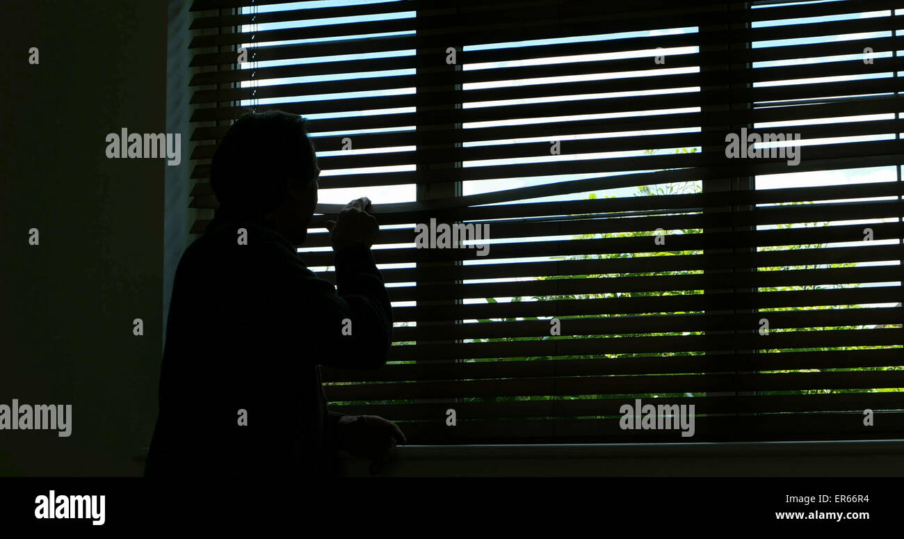 Silhouette di un irriconoscibile la persona, vista posteriore guardando fuori da una finestra cieca. Foto Stock