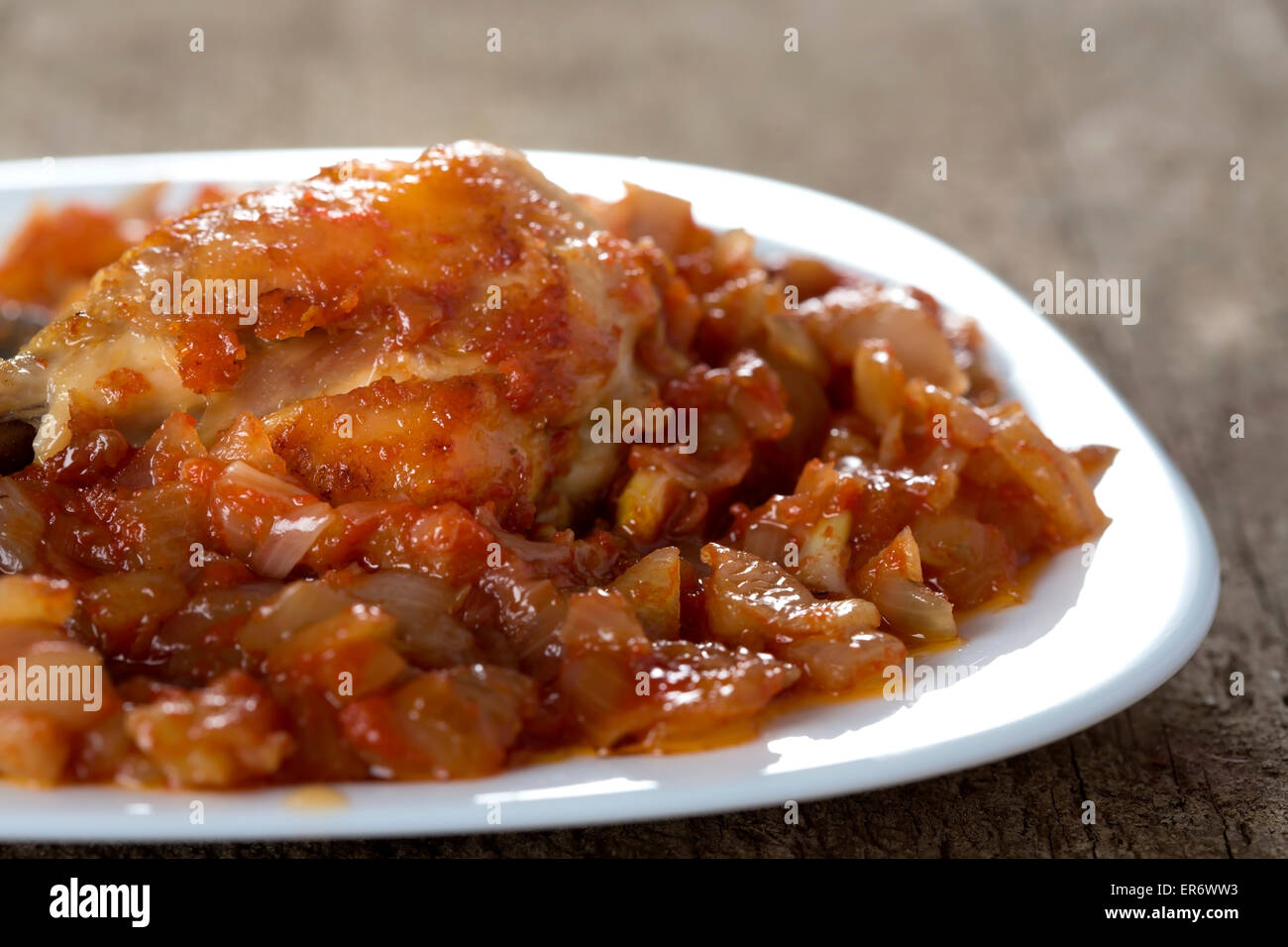 Spezzatino di pollo con salsa di cipolle in piastra bianca sul tavolo di legno Foto Stock