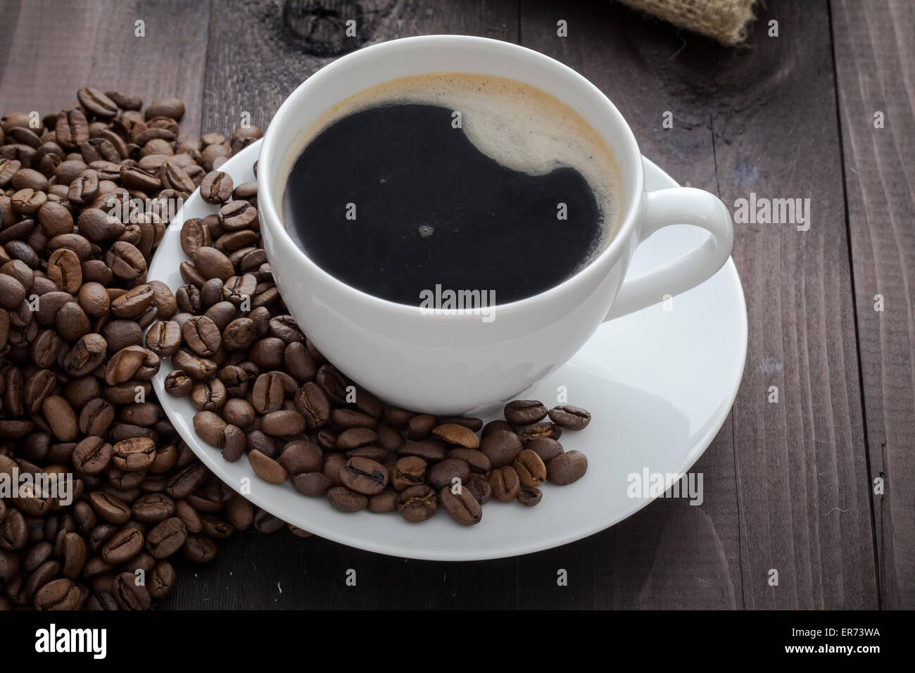 White tazza di caffè con caffè e attorno al bicchiere si trova i chicchi di caffè Foto Stock