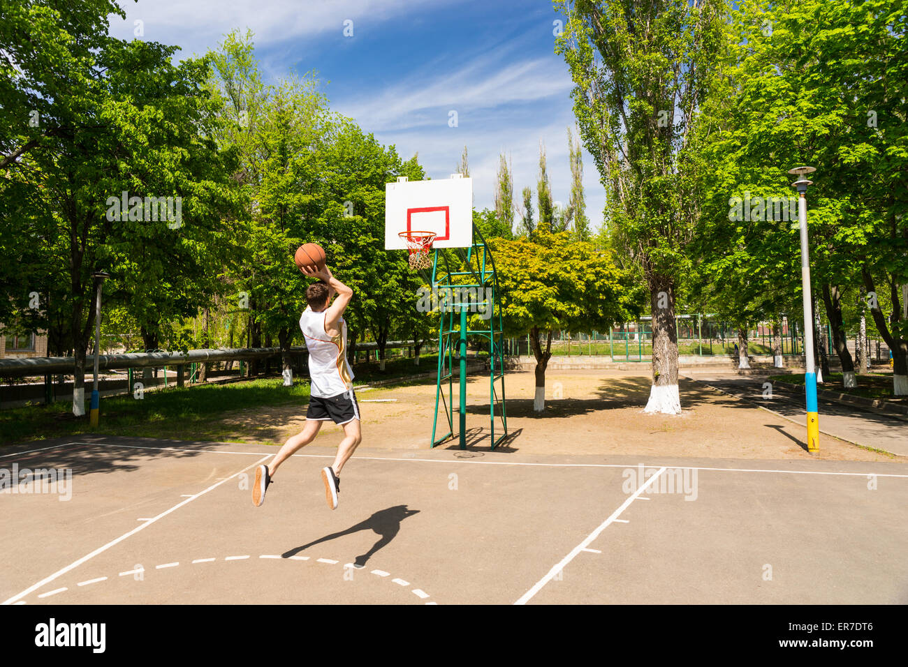 Atletica Giovane uomo prendendo jump shot dalla chiave sul campo da basket in un lussureggiante parco verde Foto Stock