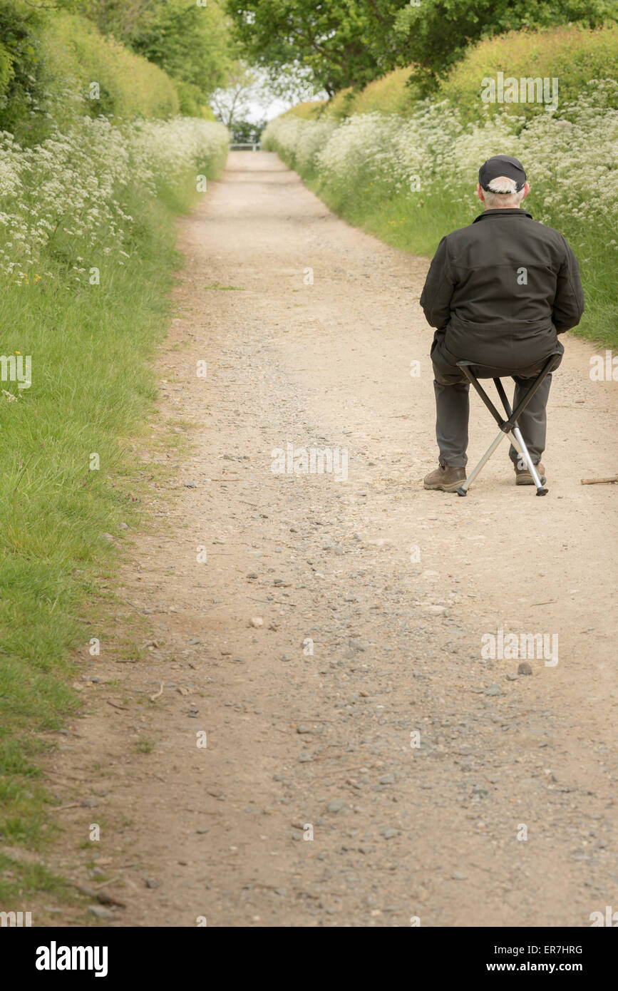 Uomo anziano si siede su uno sgabello guardando giù un percorso rettilineo. Foto Stock
