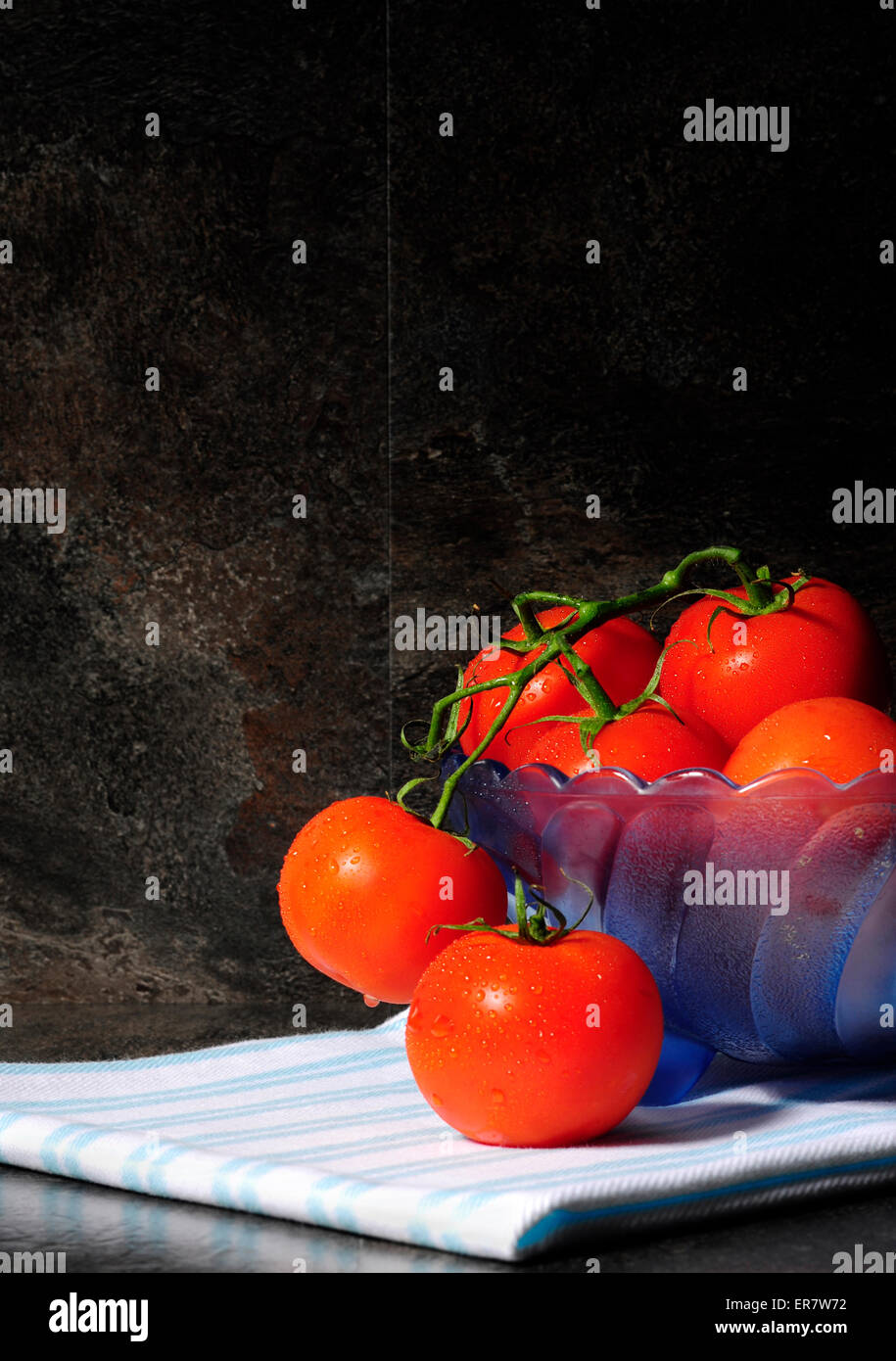 Ancora vita closeup di colore rosso brillante i pomodori in blu vintage bowl contro un drammatico nero ardesia impostazione di cucina Foto Stock