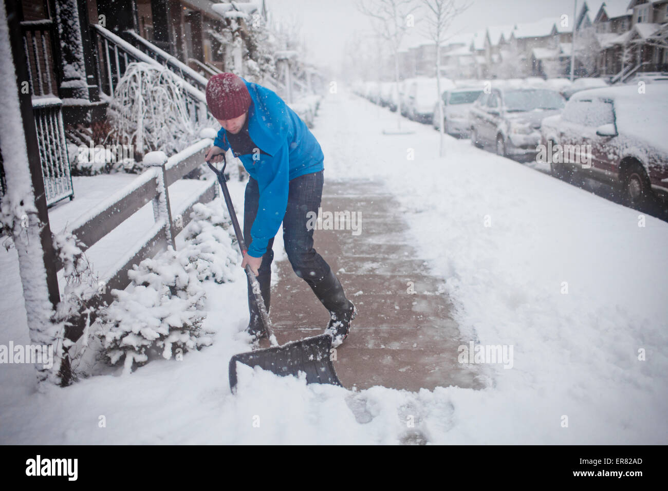 Un uomo di badili marciapiede al di fuori della sua casa suburbana. Foto Stock