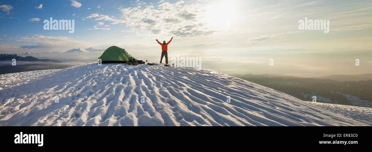 Un scalatore pone accanto alla sua tenda la mattina dopo il campeggio sulla neve in montagna. Foto Stock