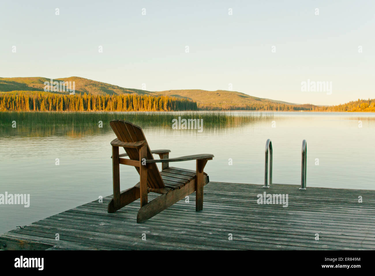Una sedia singola su un dock si affaccia verso un lago calmo in British Columbia, Canada. Foto Stock