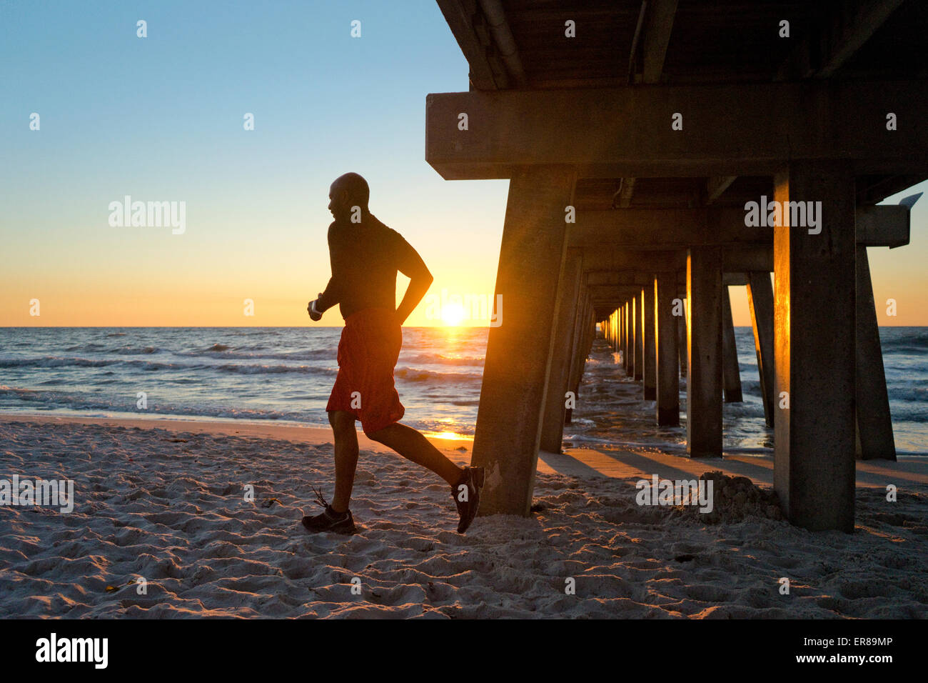 Uomo che corre sotto un molo sulla spiaggia al tramonto Foto Stock