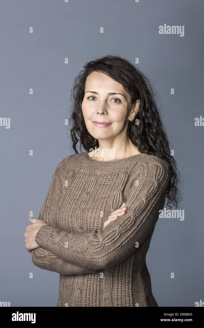 Ritratto di fiducioso donna matura in piedi con le braccia incrociate su sfondo grigio Foto Stock