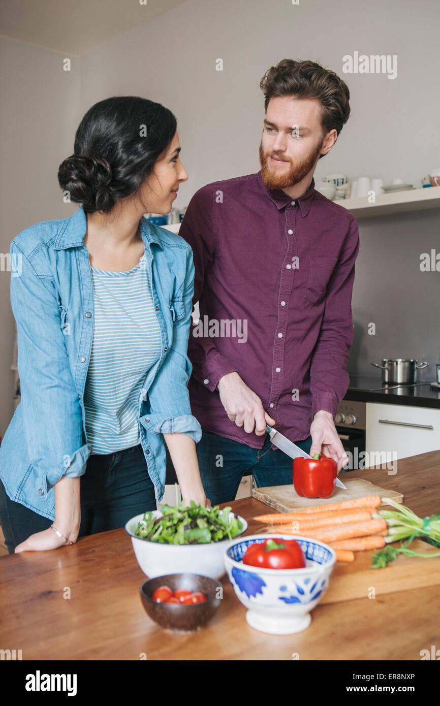 Giovane uomo tritare il peperone rosso mentre guardano la donna in cucina Foto Stock