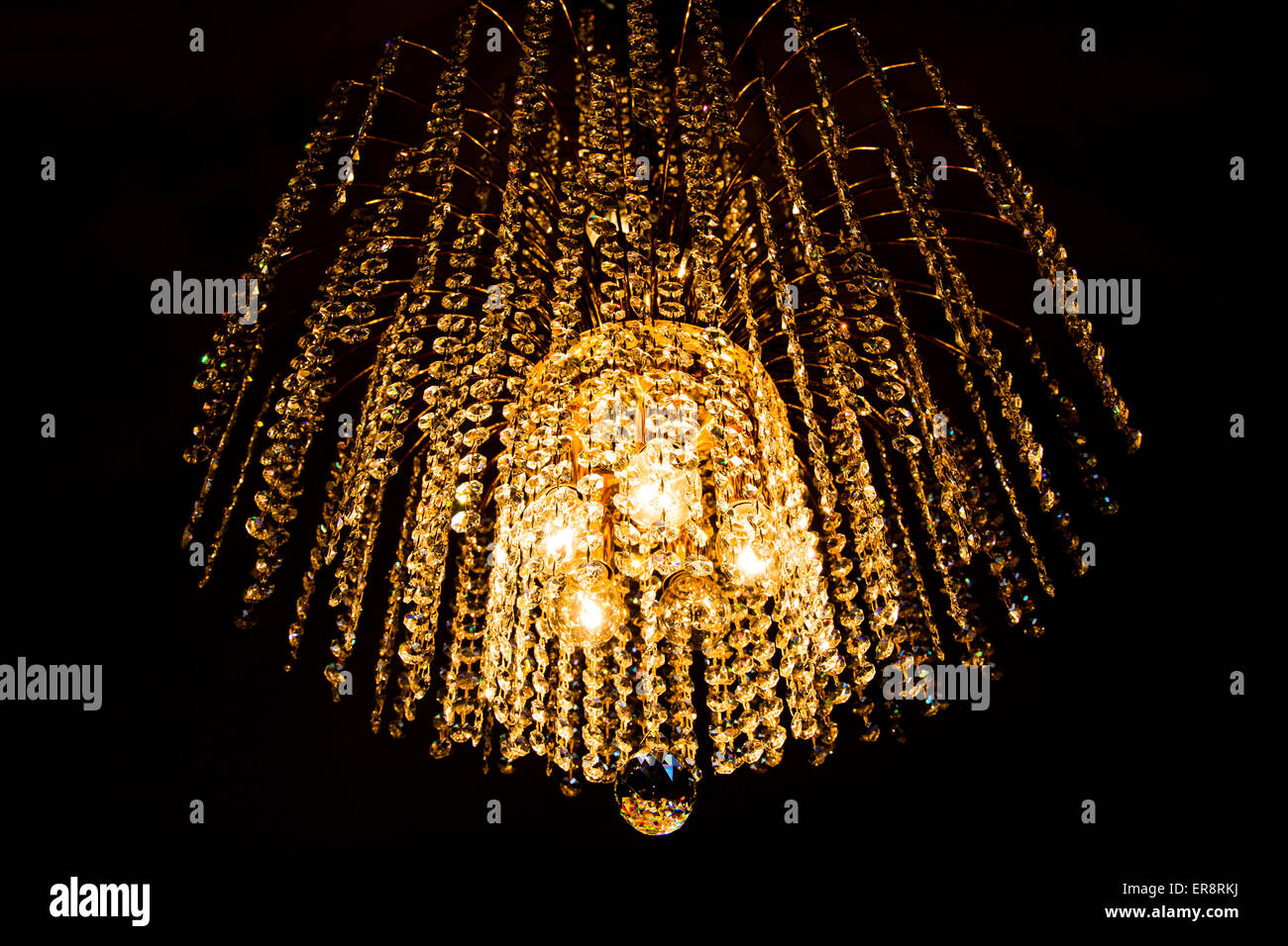 Un lampadario di cristallo si illumina con luce dorata su sfondo scuro Foto Stock