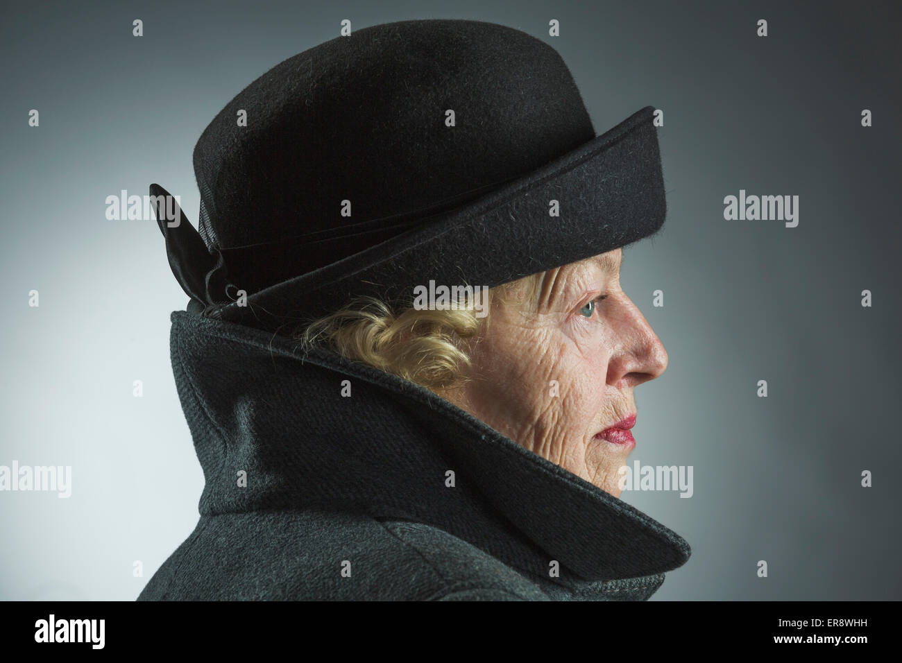 Vista laterale del senior donna che indossa un cappello e camicia contro uno sfondo grigio Foto Stock