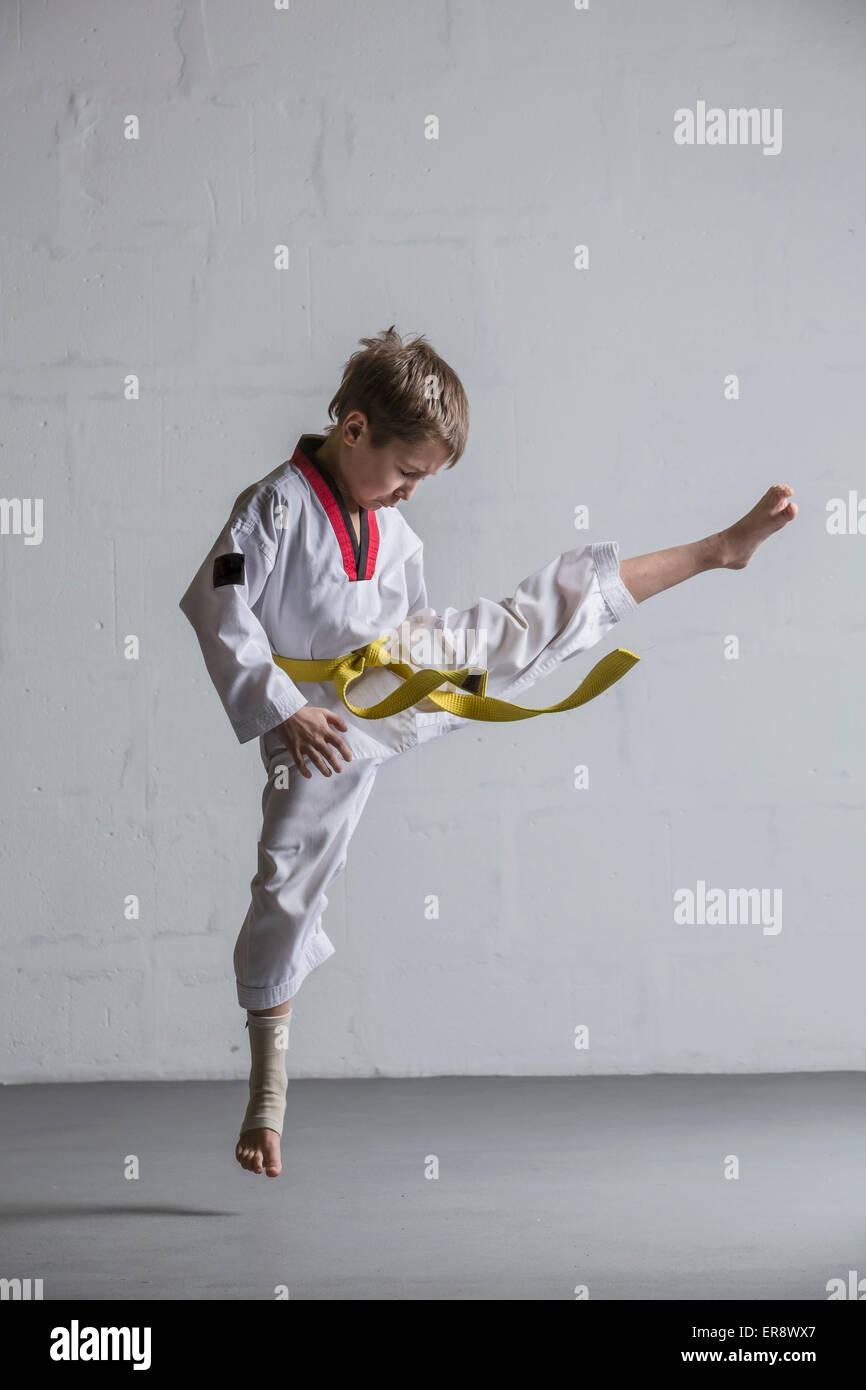 Il Karate boy calci in aria contro il muro bianco Foto Stock