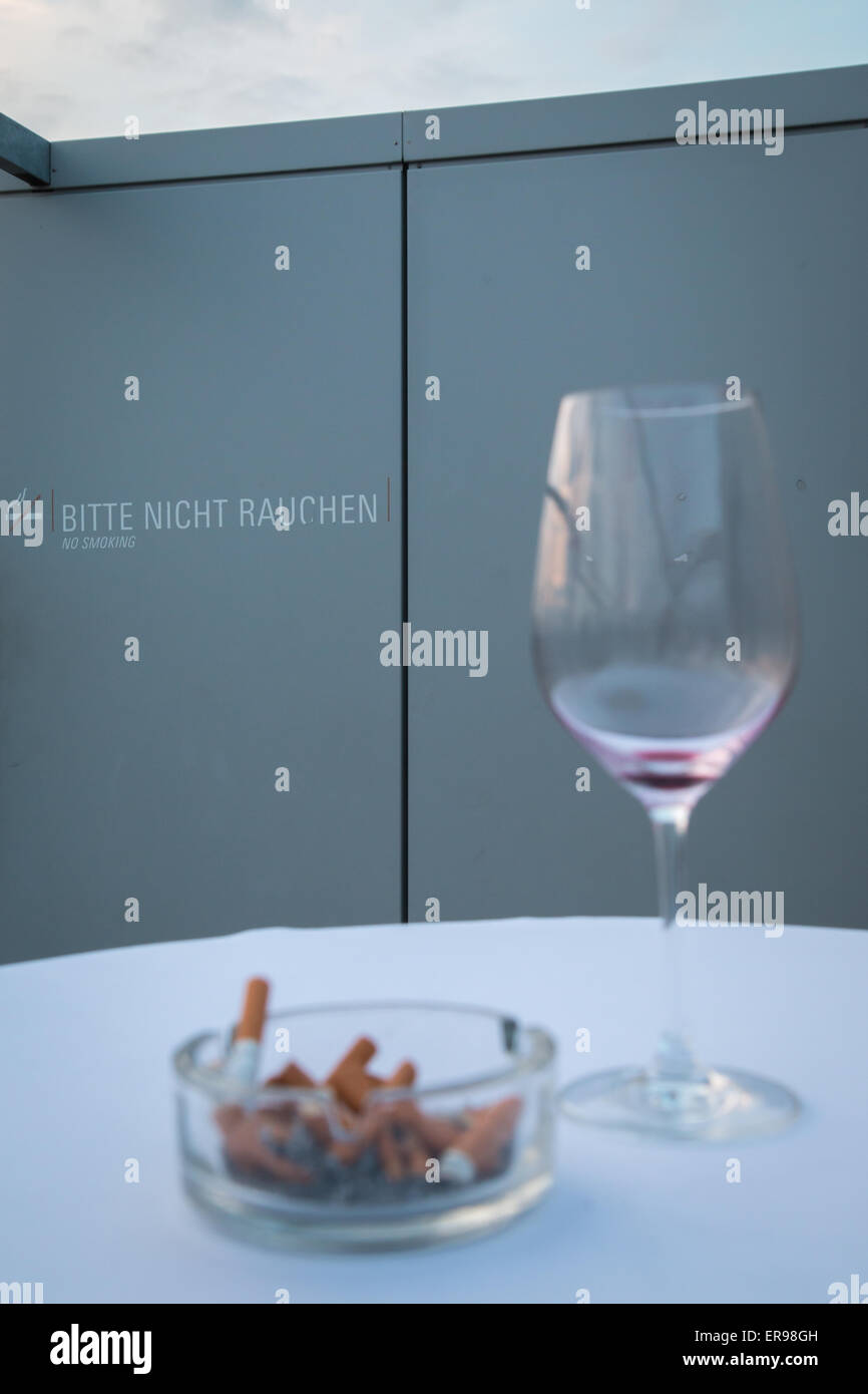Un posacenere completo e un bicchiere vuoto di vino nella parte anteriore del segno che vietano di fumare Foto Stock