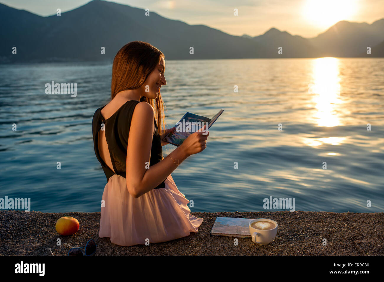 Giovane donna seduta sul molo di sunrise Foto Stock
