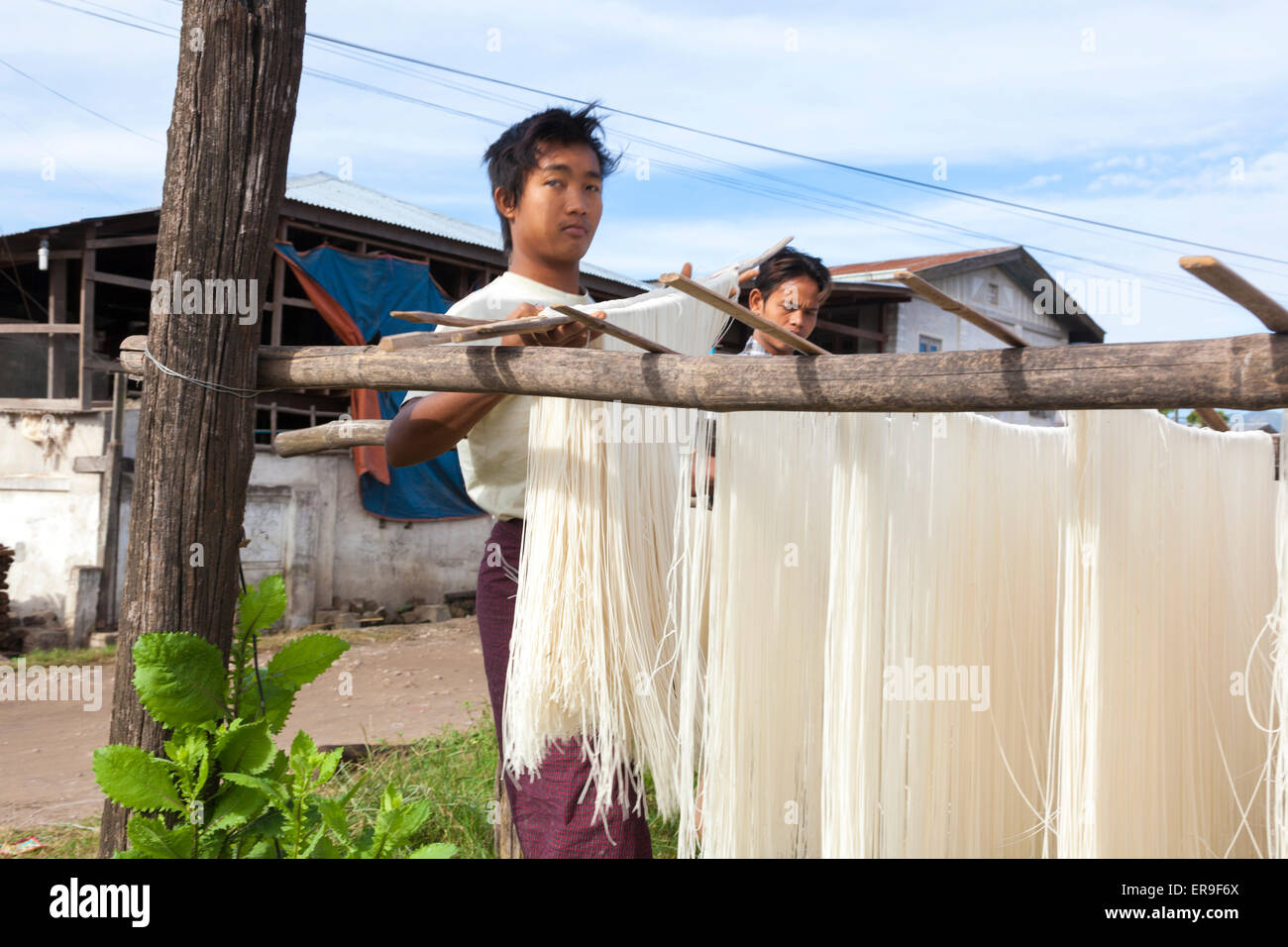 In Hsipaw, Birmania, fresca di riso tagliatelle vengono appesi su pali per asciugare all'aria aperta dopo essendo realizzati in edifici dietro. Foto Stock
