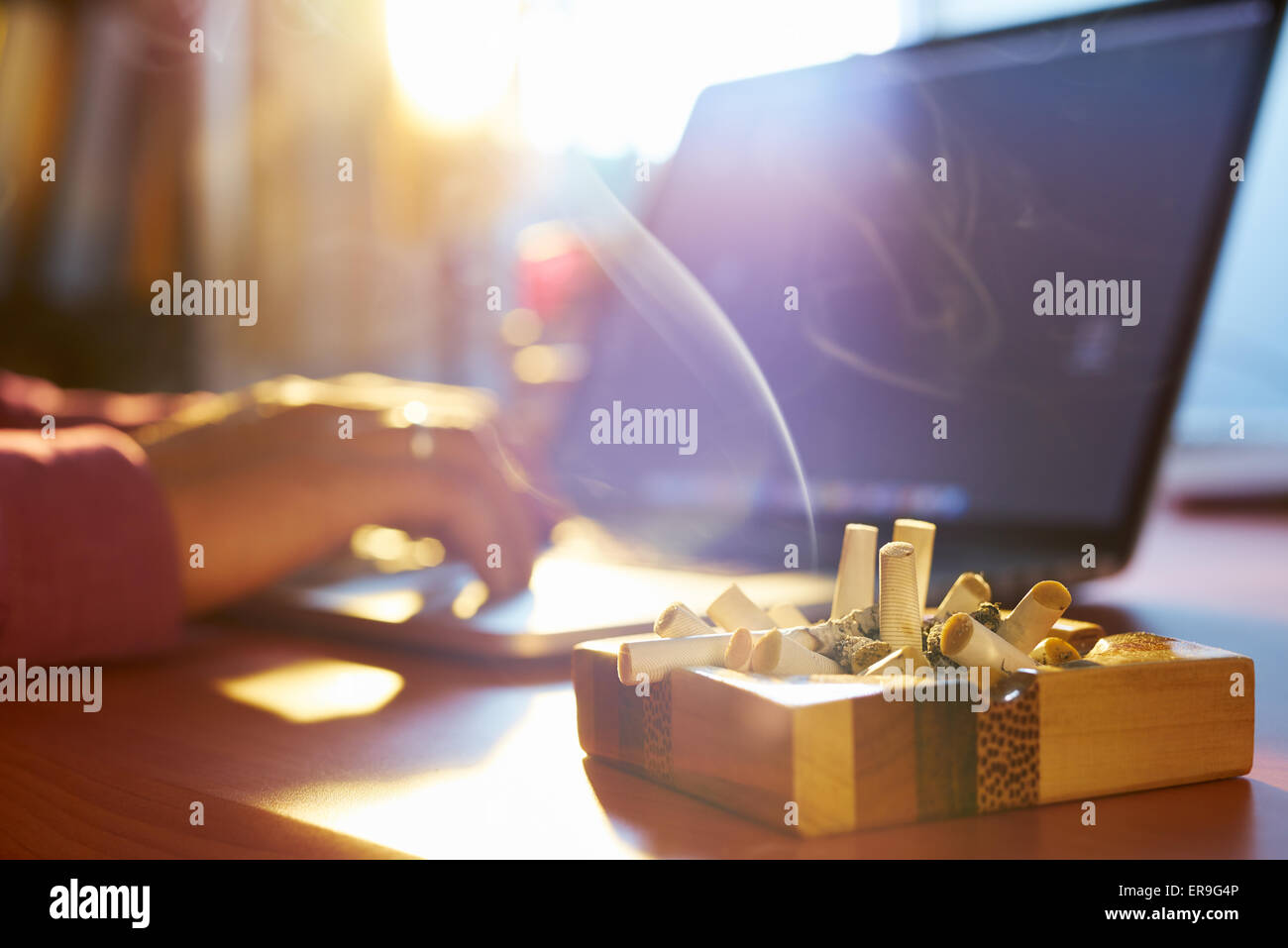 Chiusura del portacenere pieno di sigarette, con l'uomo nel lavoro in  background sul computer portatile e fumare in luoghi chiusi su la mattina  presto Foto stock - Alamy