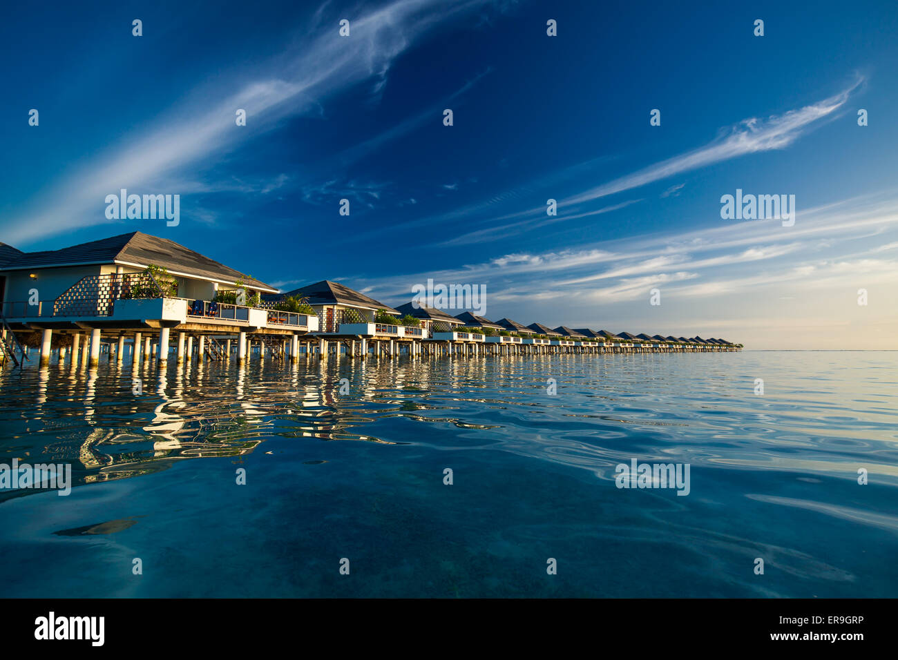 Over Water villas in Maldive riflessa nella laguna blu prima del tramonto Foto Stock