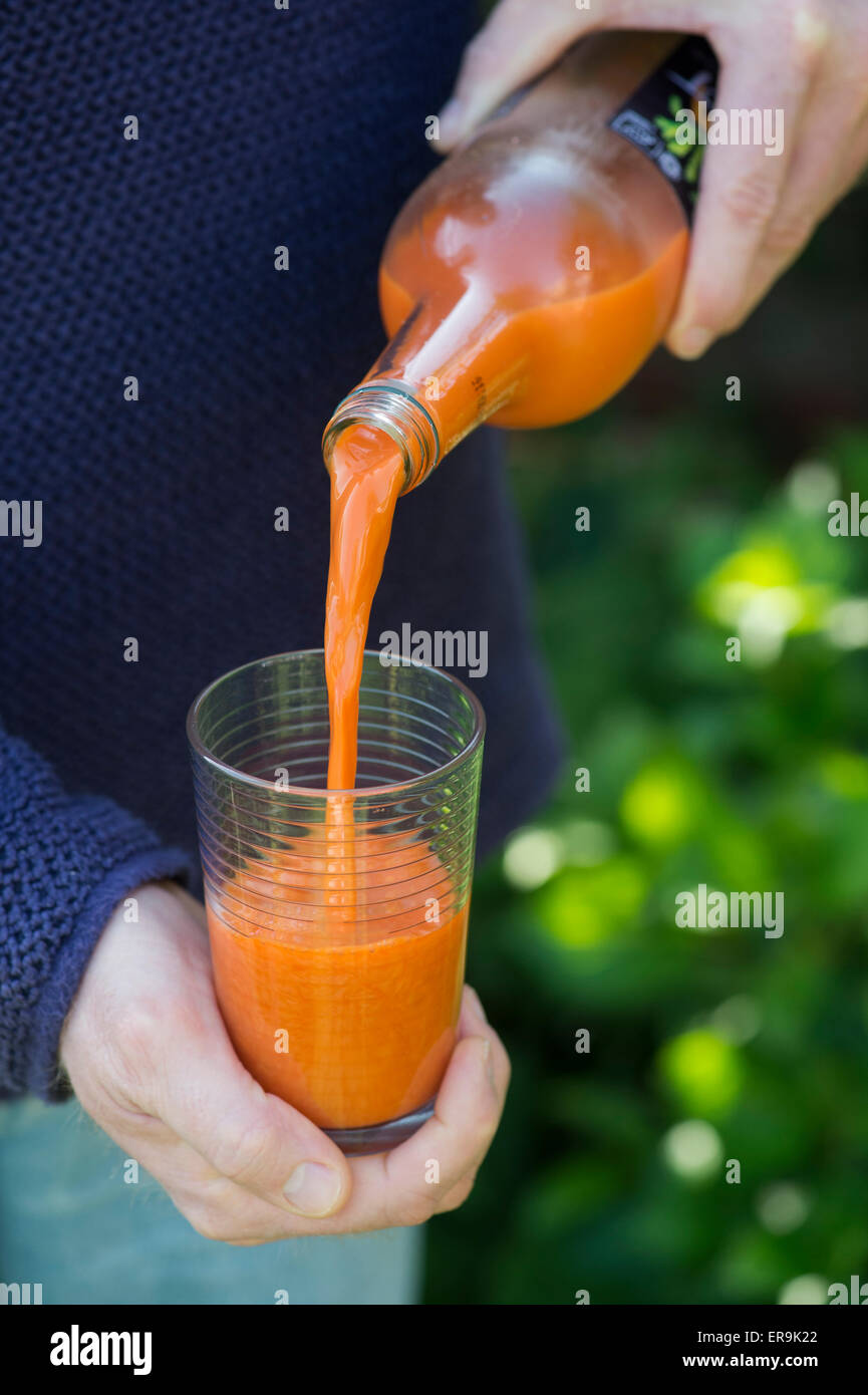 Versare il succo di carota in un bicchiere Foto Stock