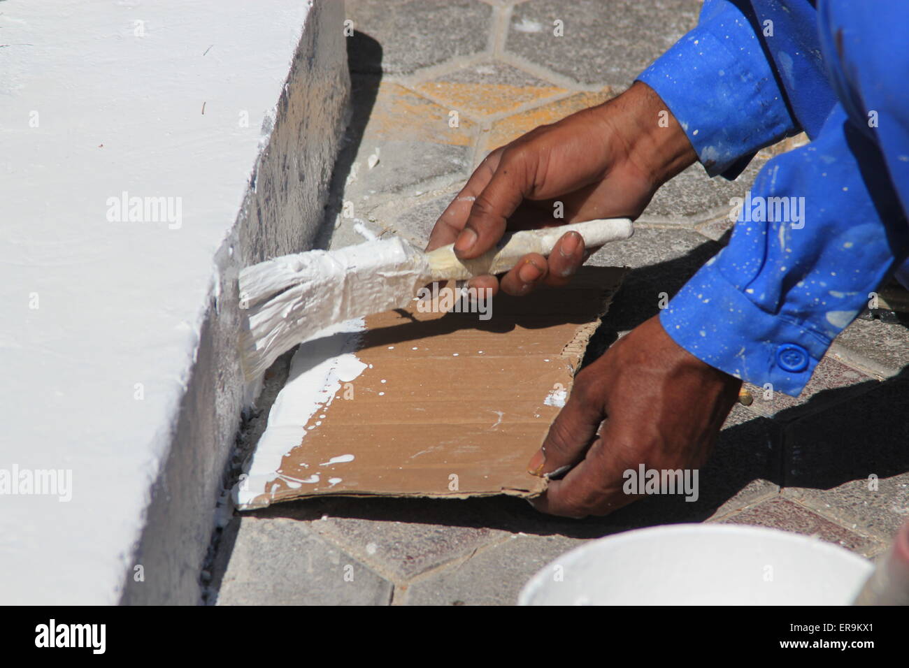 Un pittore in tute blu dipinto un percorso con vernice bianca che simboleggia la pittura e decorazione, manutenzione stradale, lavoratore manuale Foto Stock