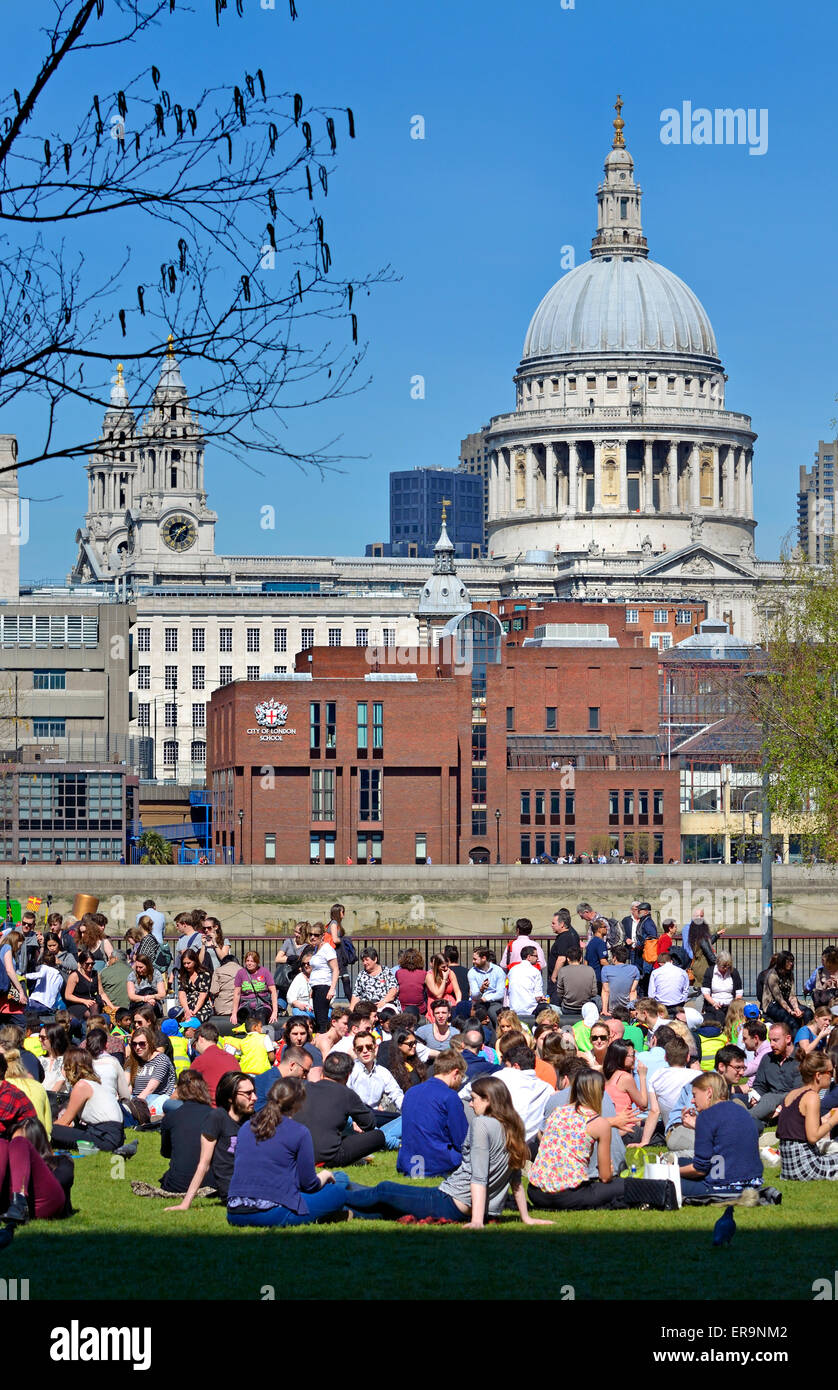 Londra, Inghilterra, Regno Unito. La gente seduta nel sole fuori la Tate Modern sulla banca del sud. La Cattedrale di St Paul e dietro Foto Stock