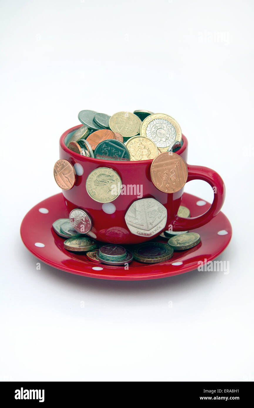 'My cup corre su un bicchiere di bianco e il piattino pieno di GBP British monete fuoriuscita.Un REGNO UNITO denaro economia finanza monete ricchezza Foto Stock