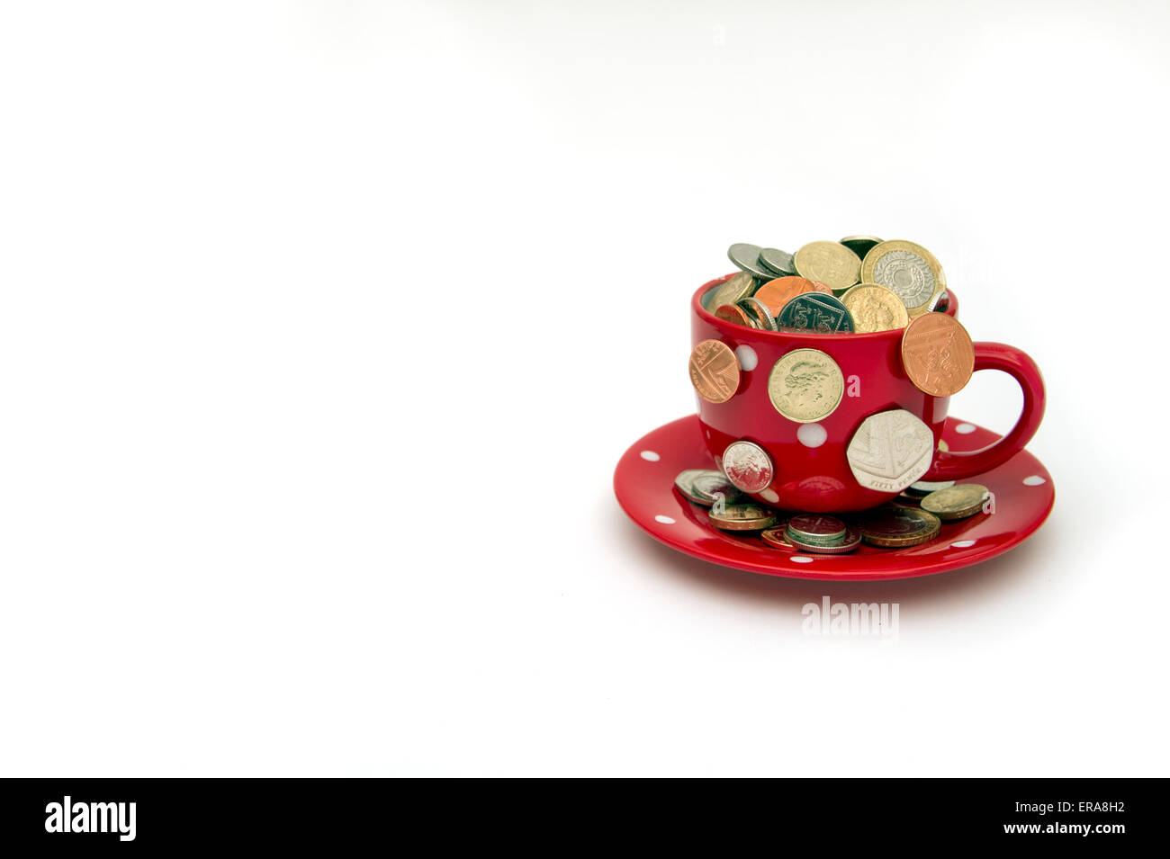 'My cup corre su un bicchiere di bianco e il piattino pieno di GBP British monete fuoriuscita.Un REGNO UNITO denaro economia finanza monete ricchezza Foto Stock