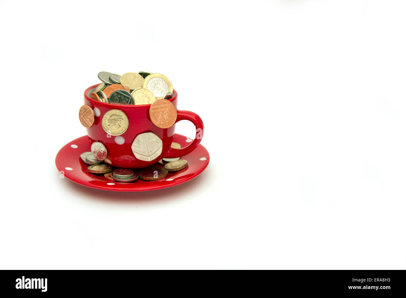 'My cup corre su un bicchiere di bianco e il piattino pieno di GBP British monete fuoriuscita.Un REGNO UNITO denaro economia finanza monete ricchezza Foto Stock