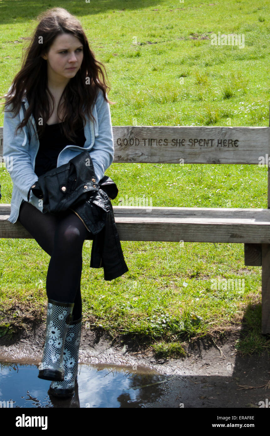 Una giovane ragazza seduta su una panchina nel parco ("Good Times ha trascorso qui') da soli con una malinconia o perfino tristi o depresse espressione. Foto Stock