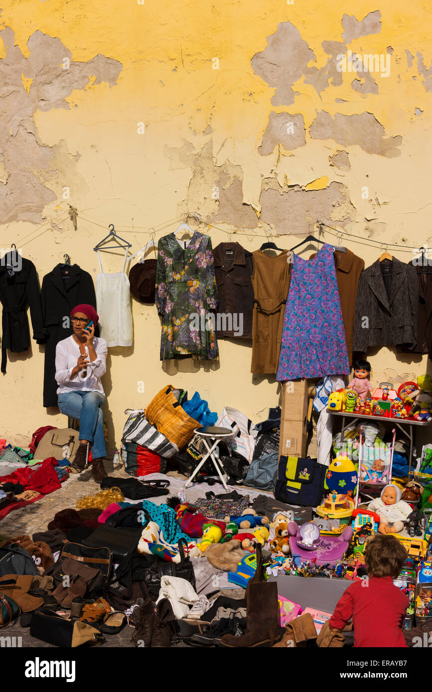 Donna al telefono circondare con la sua mercanzia per vendita a Feira da Ladra, ladri o mercato. Foto Stock