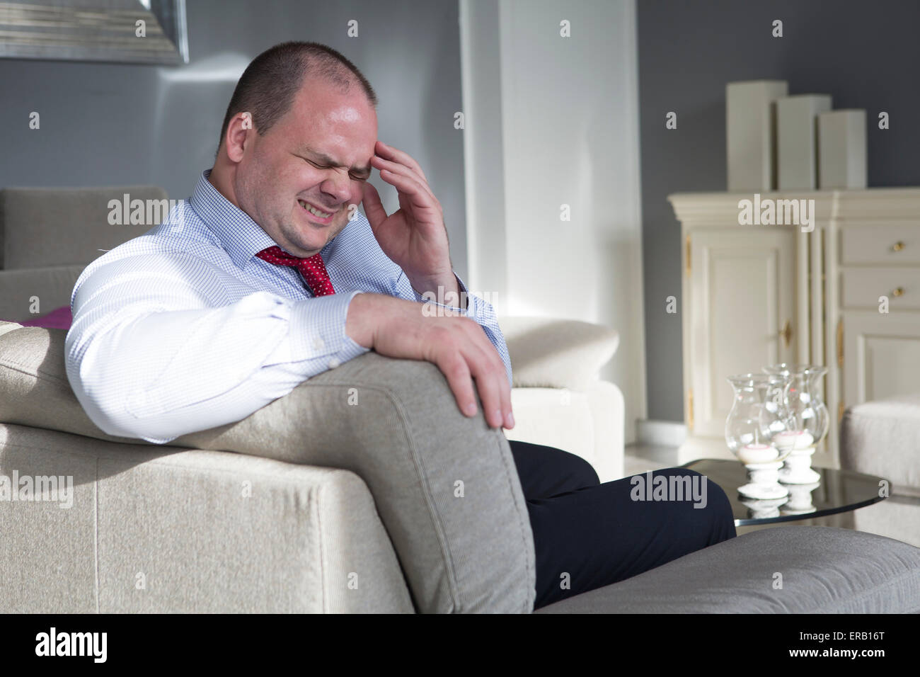 Uomo in camicia e cravatta si siede sul divano con un mal di testa Foto Stock
