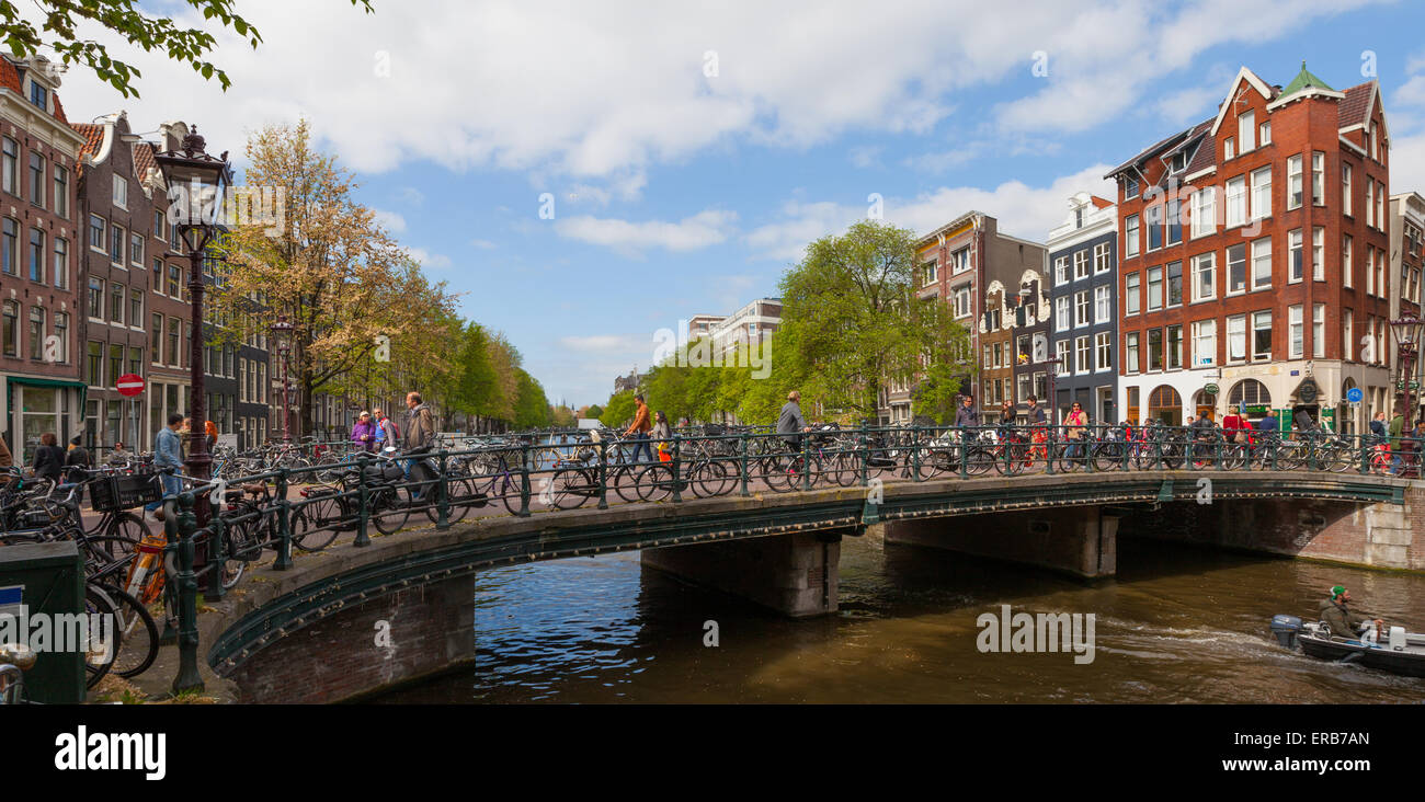 Vista panoramica del ponte sul fiume Amstel con persone e biciclette e cielo blu in background in Amsterdam. con le persone. Foto Stock