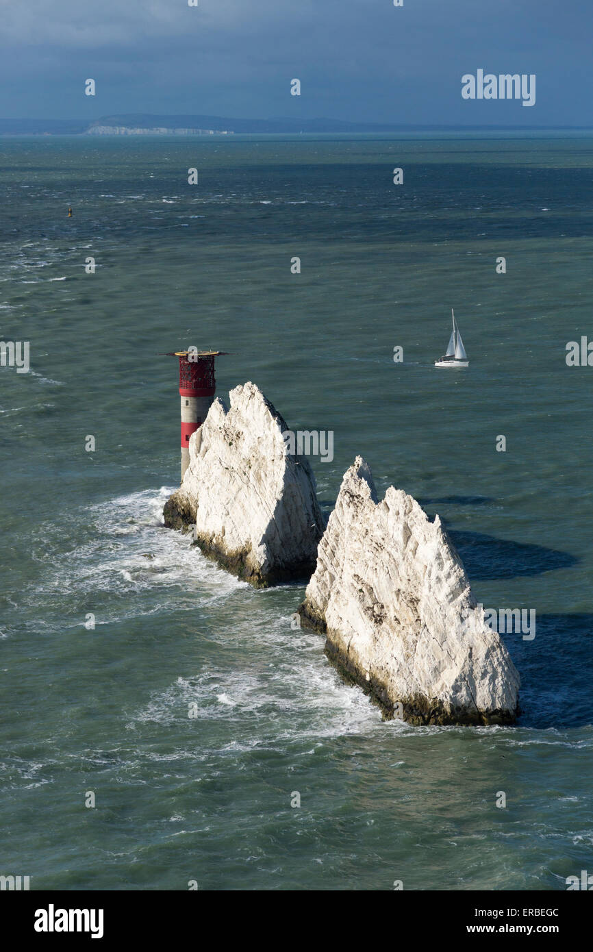 Il gesso Needles e Needles Lighthouse illuminato dal sole con un suggestivo cielo tempestoso e una barca a vela in autunno, Isola di Wight, Regno Unito Foto Stock