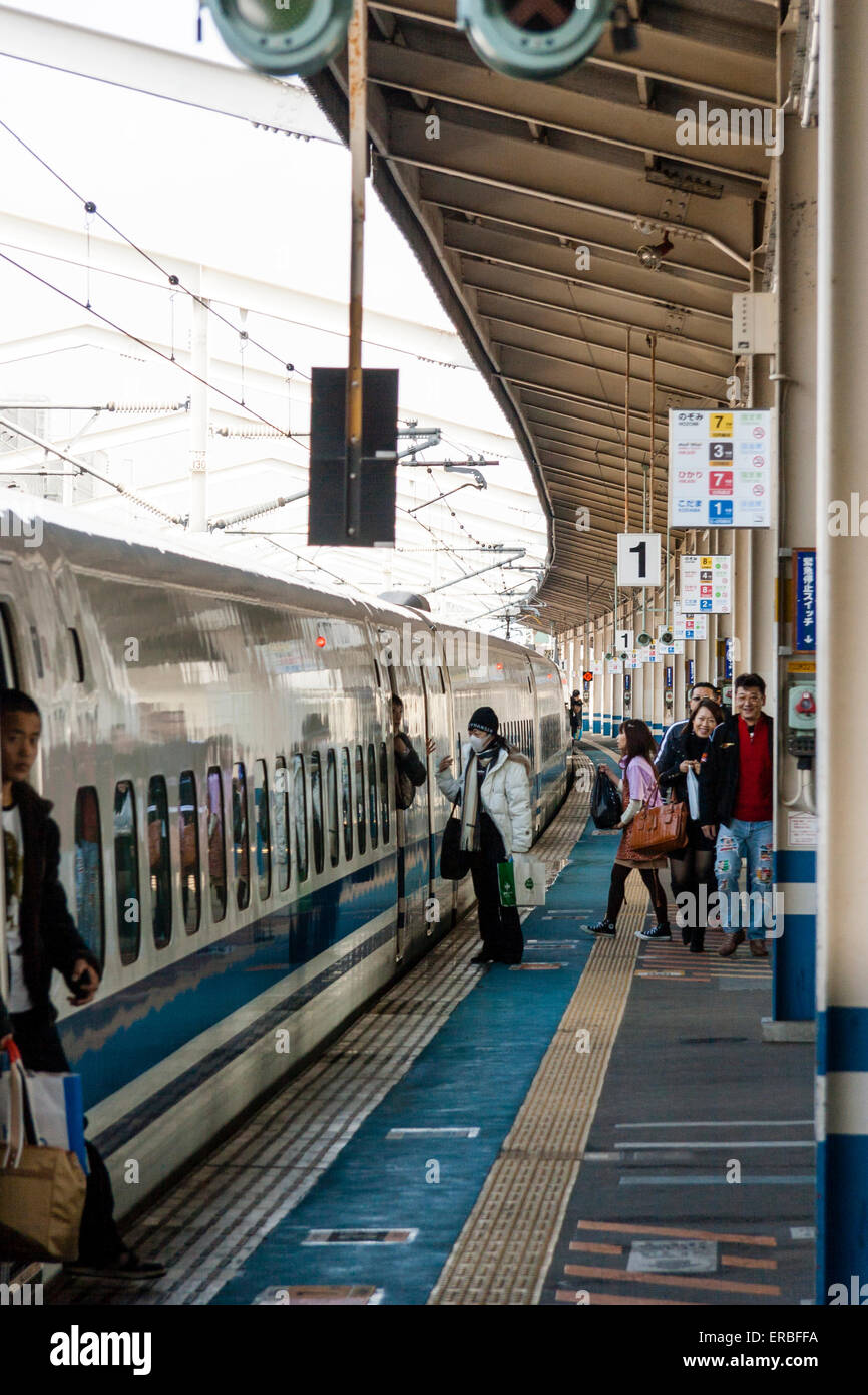 La gente che scola da un treno superveloce giapponese della serie 700 Shinkansen alla stazione di Fukuyama con i passeggeri in partenza che aspettano sul binario. Foto Stock